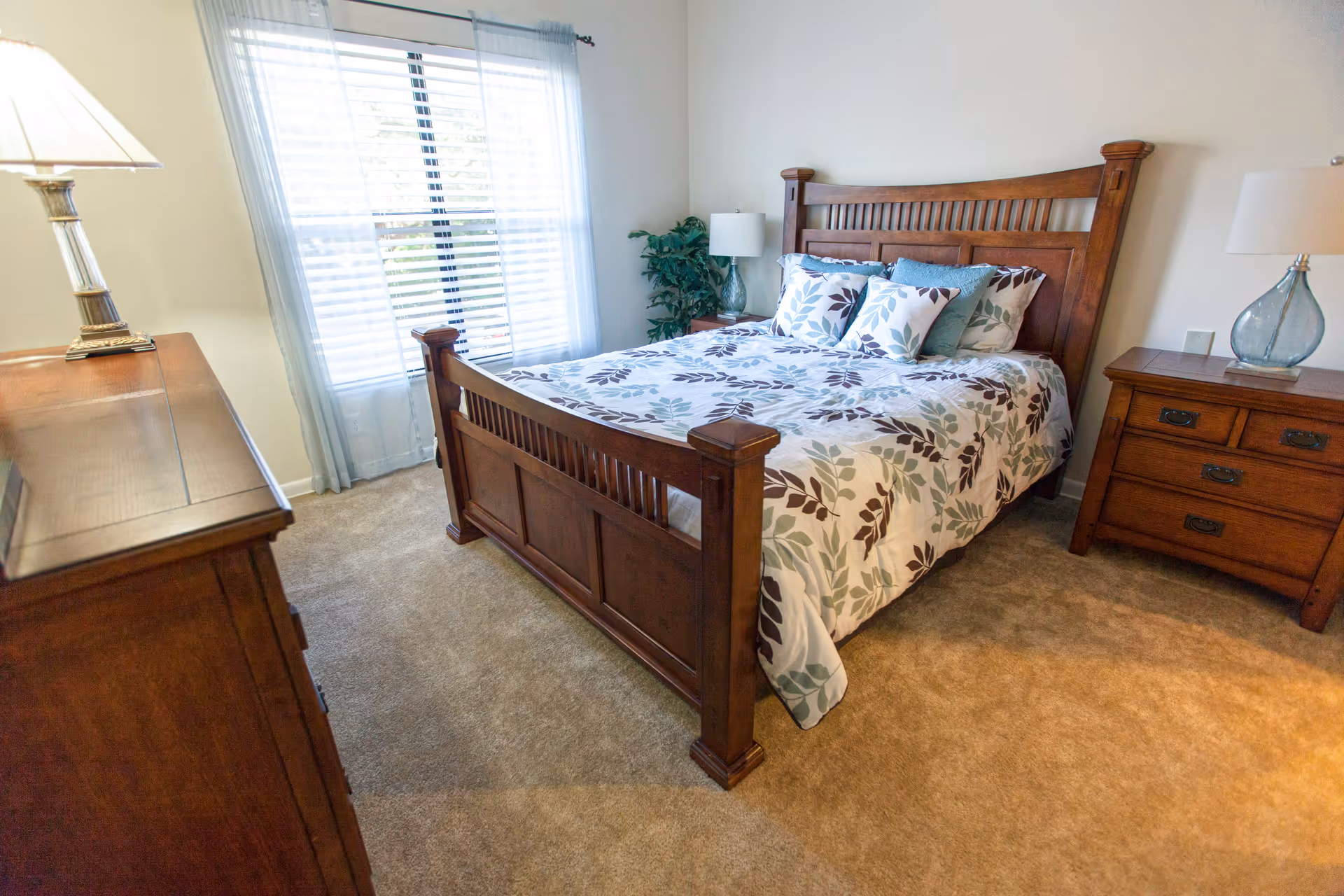 Wooden bed with matching dressers and lamps in a bright, neatly furnished bedroom.