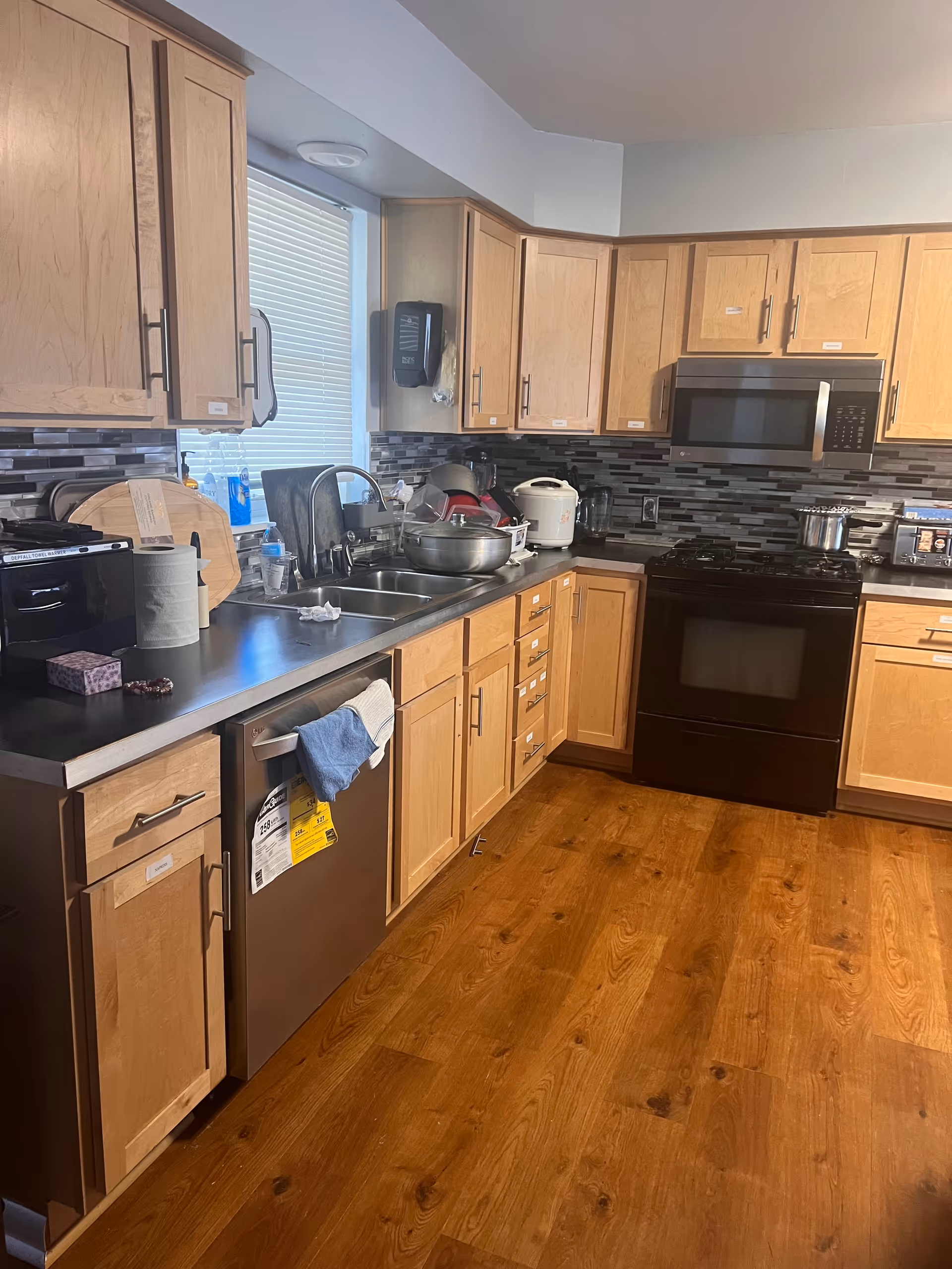 Wooden-cabinet kitchen with stainless appliances, sink, and cluttered countertops.