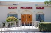 The exterior of Saint Francis Home shows a beige building with red lettering and wooden doors.