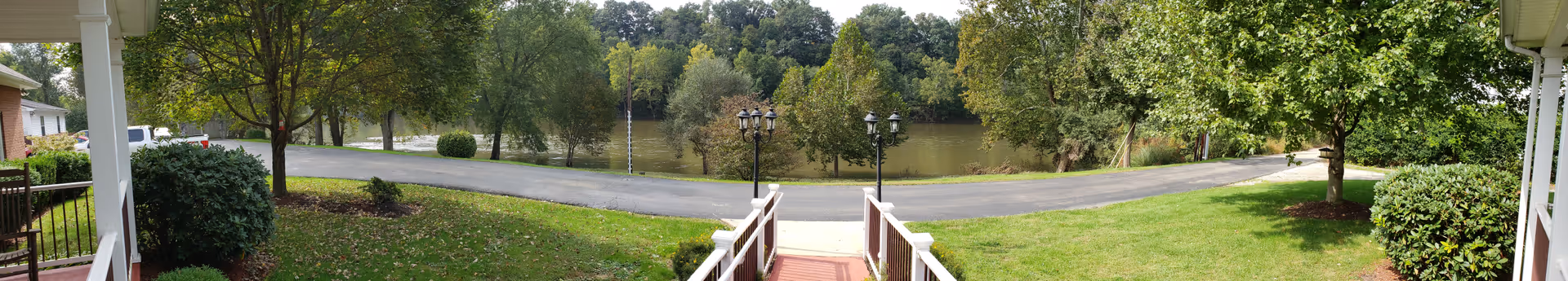 Panoramic outdoor view of a lawn, path, trees, and a lake by the facility.