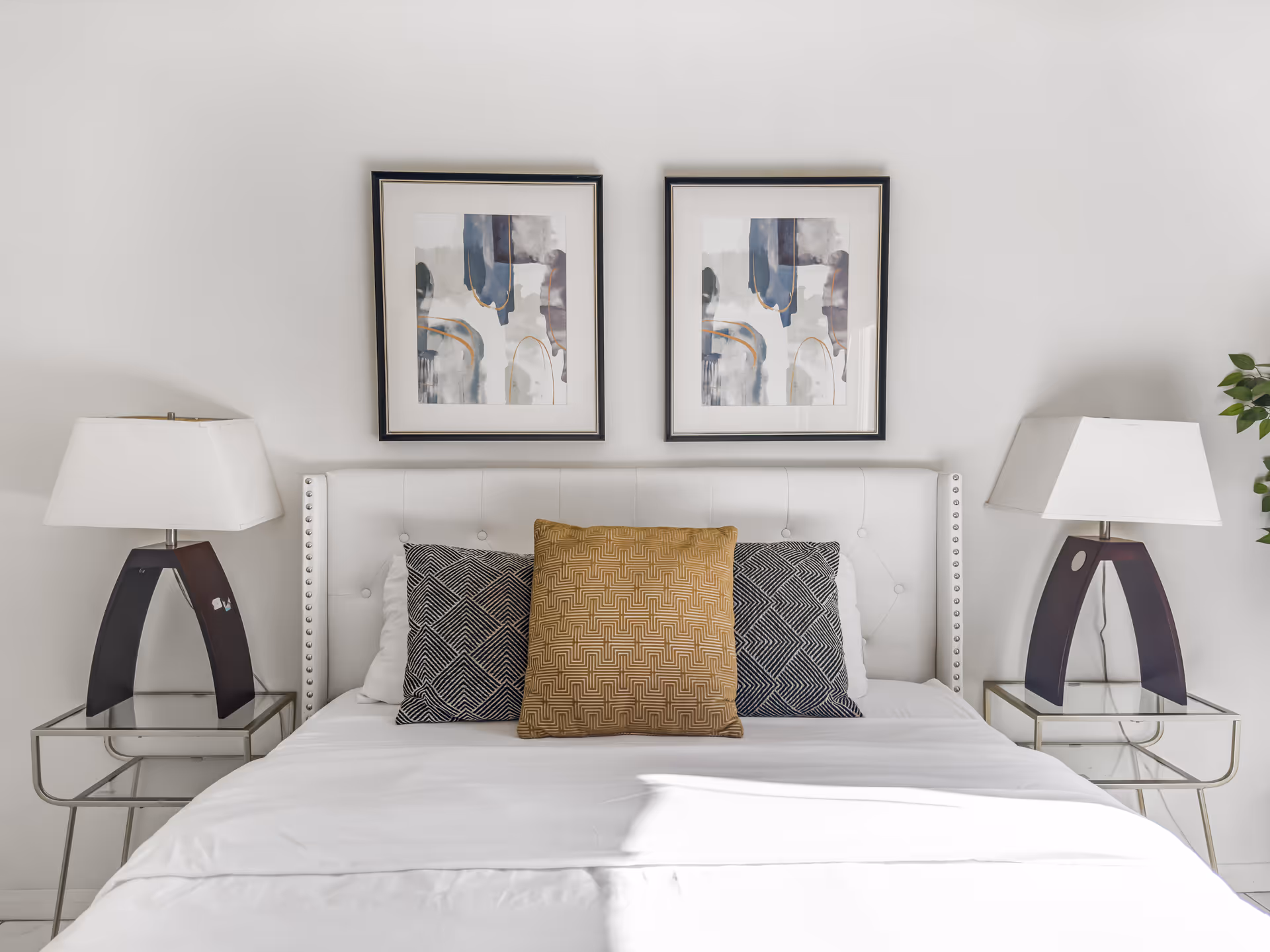 White upholstered bed with patterned pillows, two lamps, and framed art above.