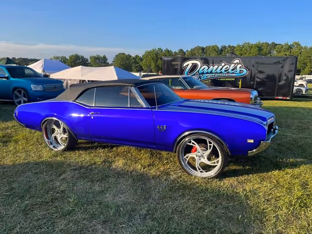 A vivid blue vintage convertible parked on grass at an outdoor car show.
