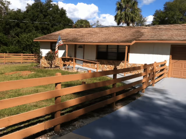 Single-story assisted living residence with a wooden fence, front porch ramp and an American flag.
