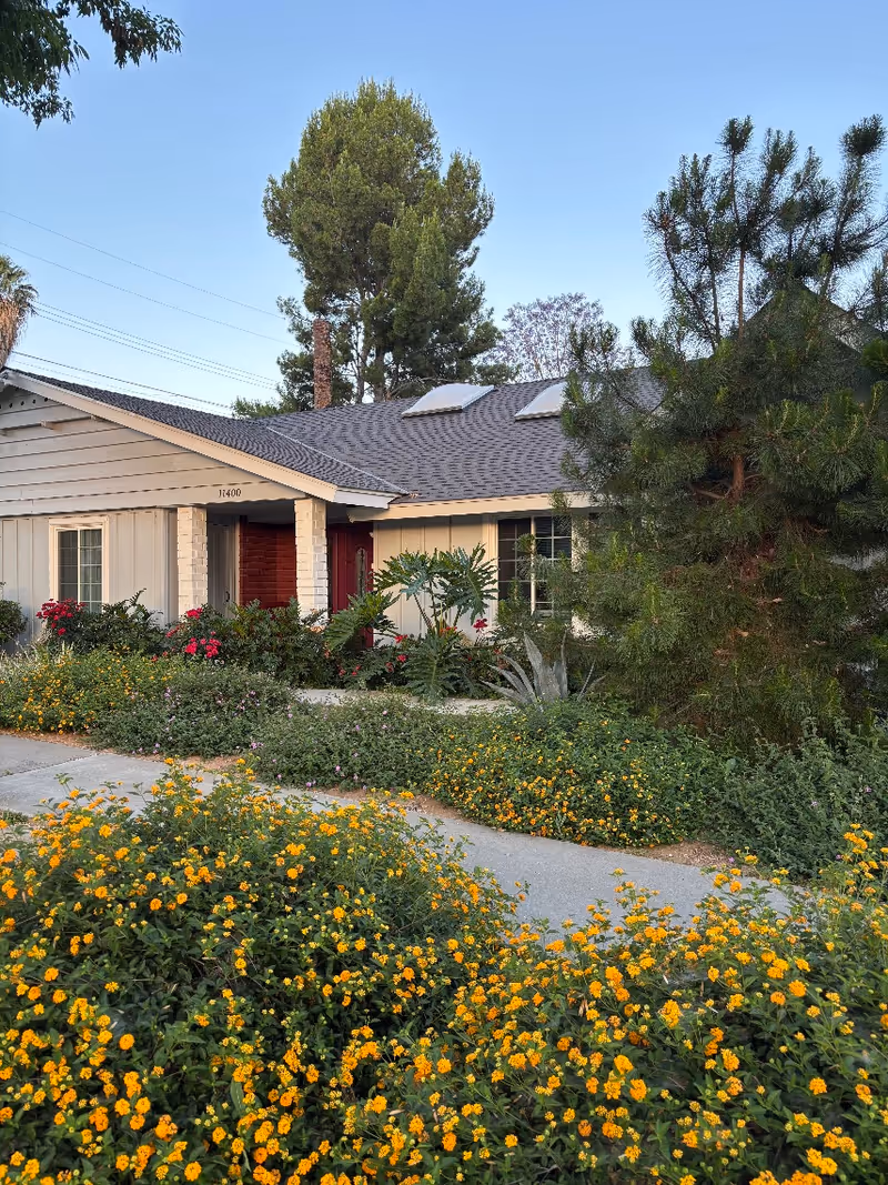 Exterior view of a single-story Excelcare facility with colorful flower beds and a walkway.