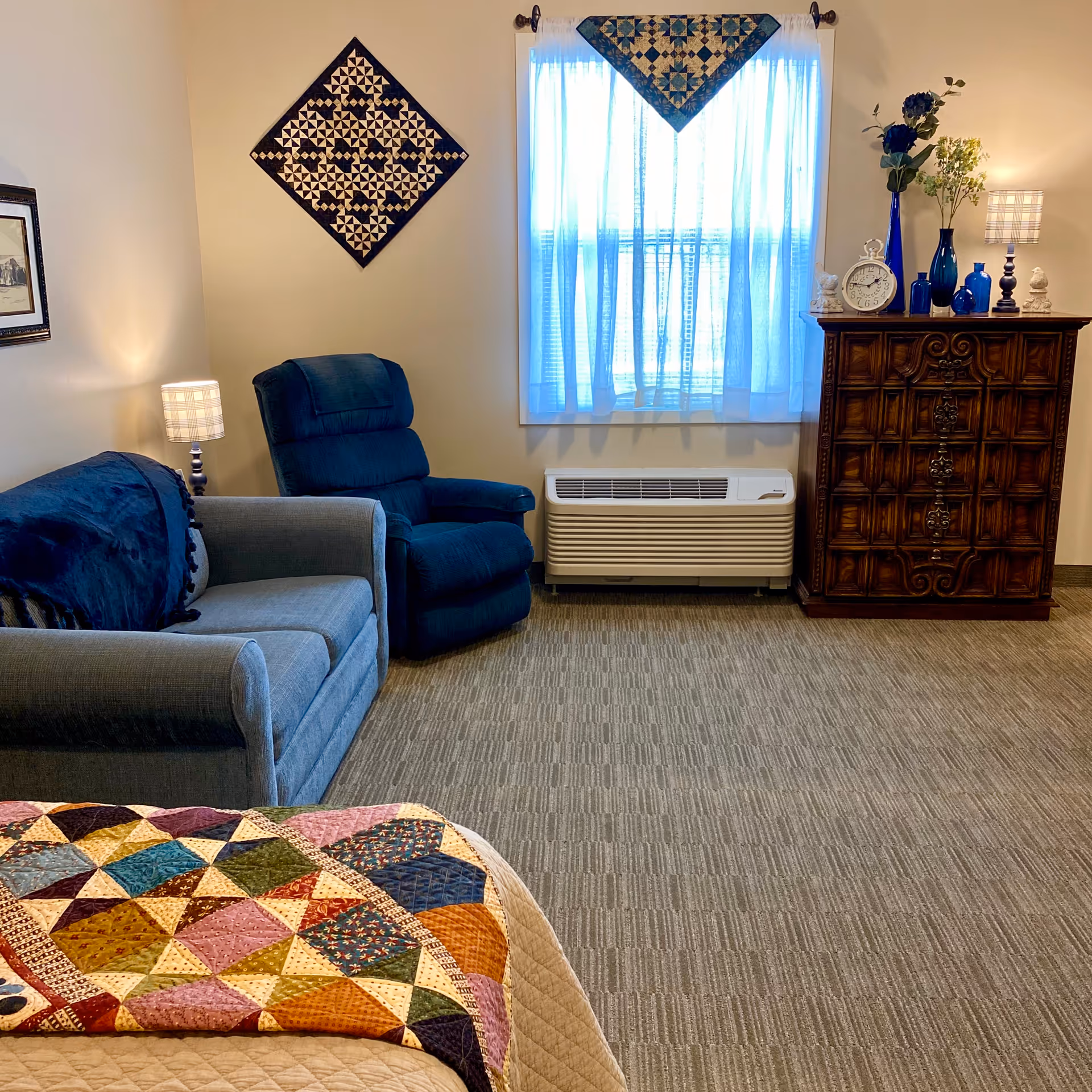 Cozy living room with blue recliner, sofa, window curtains, and a wooden dresser.