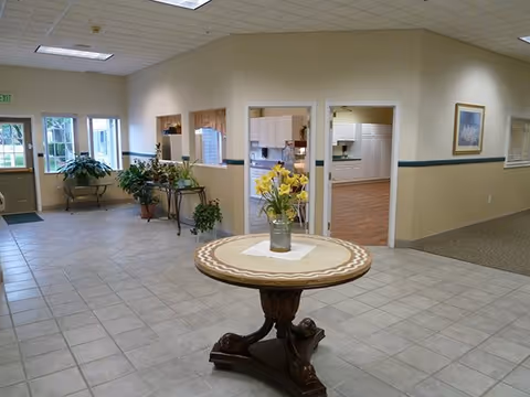 Spacious lobby area with a round pedestal table, vase of flowers, and potted plants.