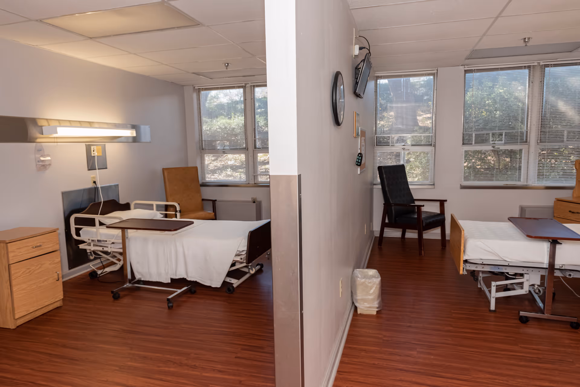 Two hospital-style beds and chairs in a shared patient room with divider