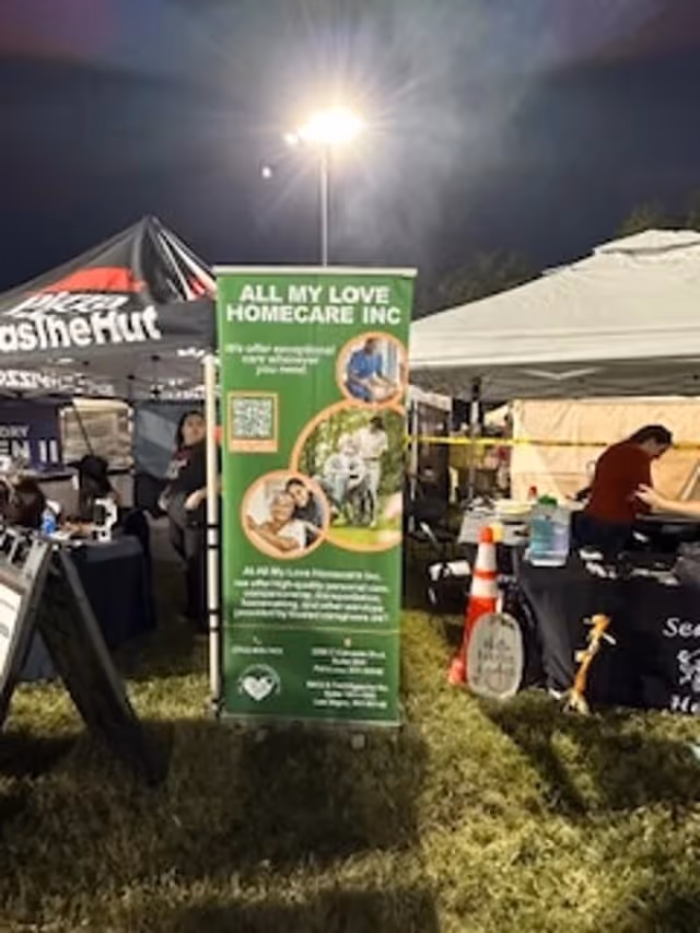 Outdoor event booth setup featuring All My Love Home Care banner under tents at night