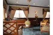 A cozy senior living room with couches, chairs, a coffee table, curtains, and a floral arrangement.