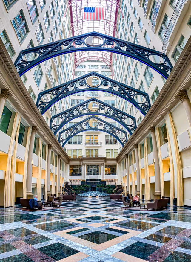 Grand indoor atrium with ornate blue arches, skylight, and marble-patterned floor.