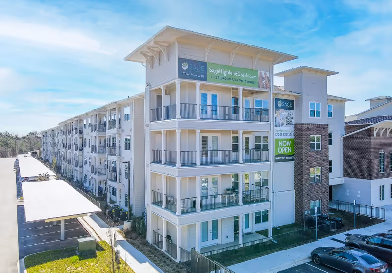 Exterior view of Sage Highland Creek senior living building with balconies and a Now Open banner.