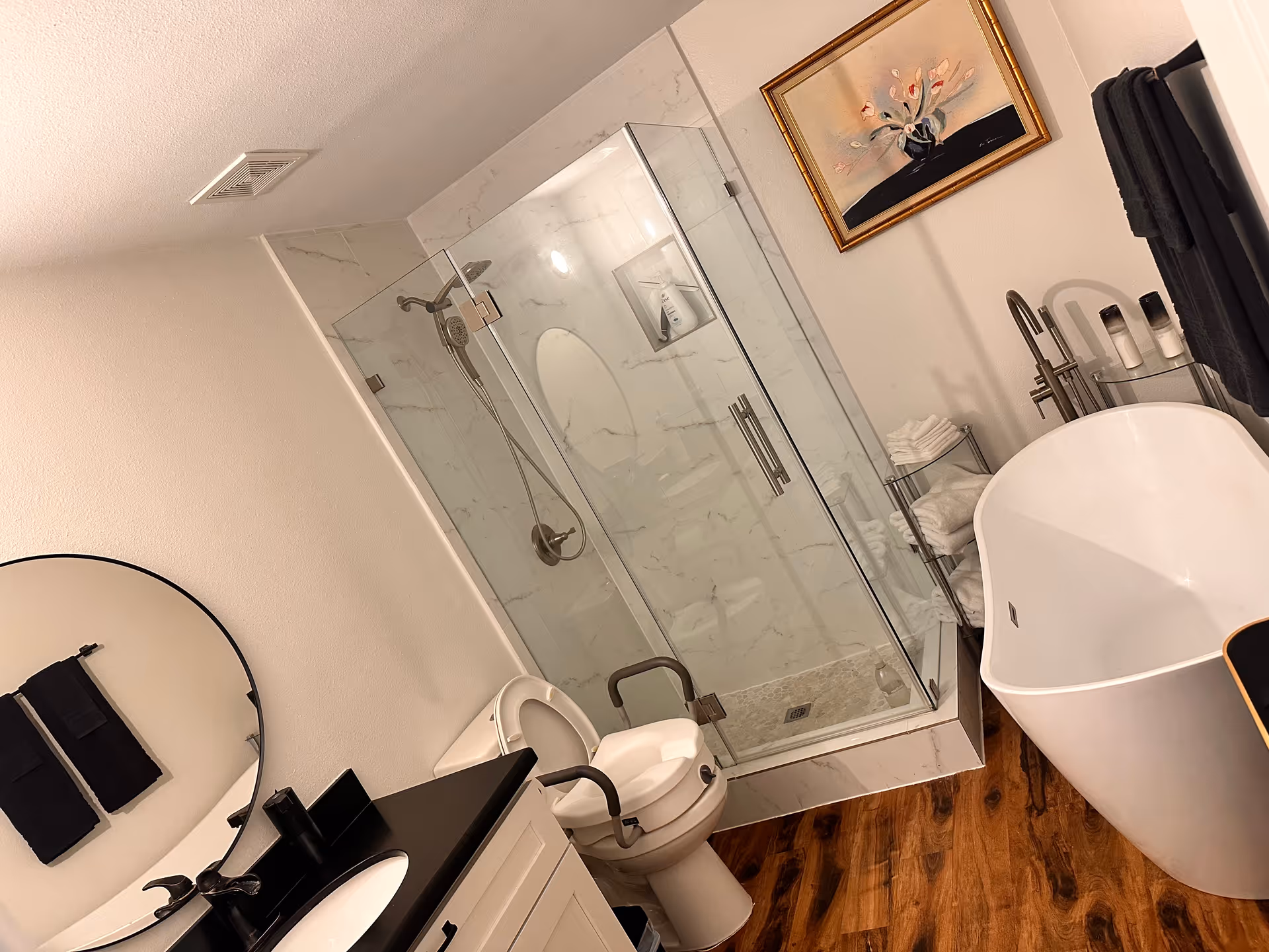 Modern bathroom with glass-enclosed shower, freestanding tub, and round mirror.