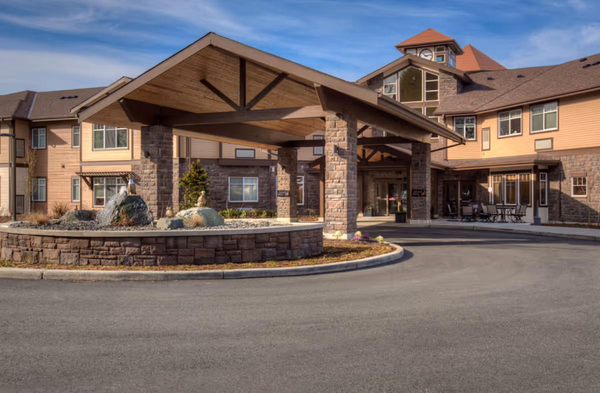 Senior living facility exterior with stone pillars, porte-cochere, and circular driveway.