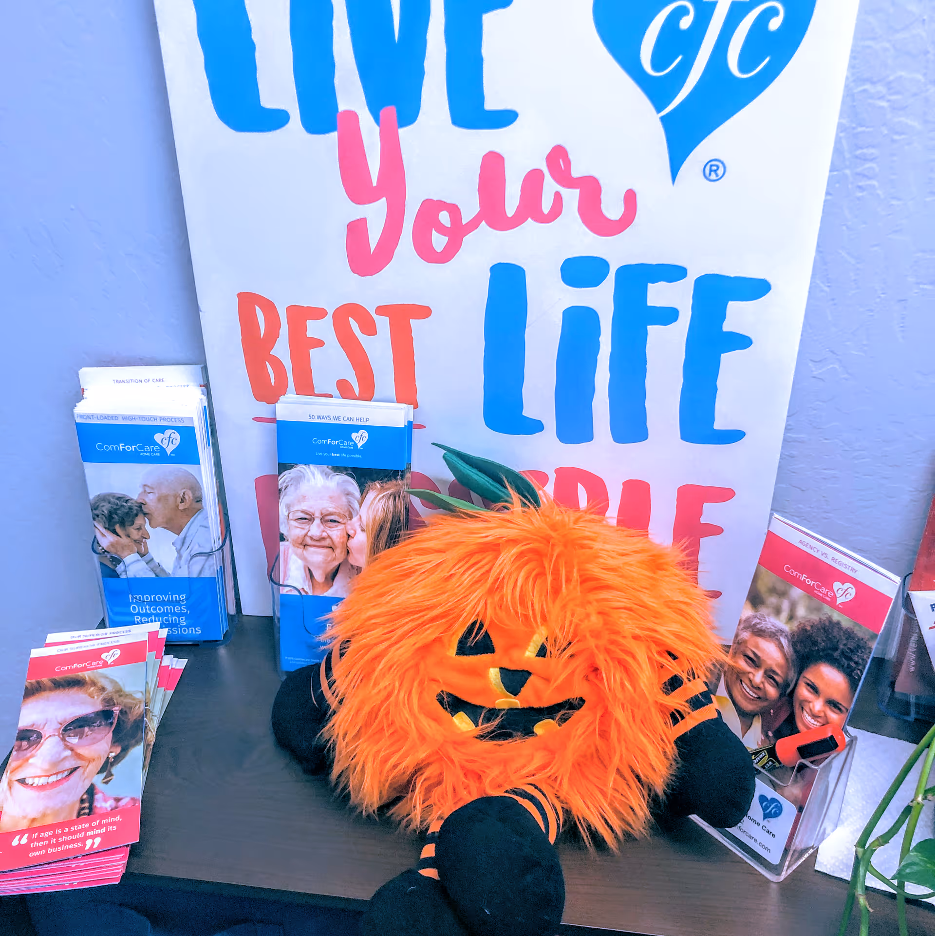 Promotional display with brochures, banner reading 'Live Your Best Life,' and a pumpkin plush on table.
