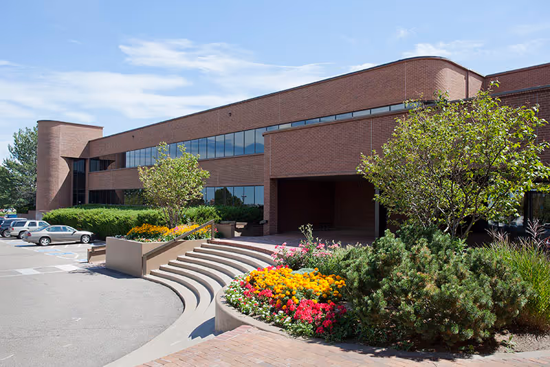 Brick senior living facility exterior with landscaped entrance, steps, and blue sky.