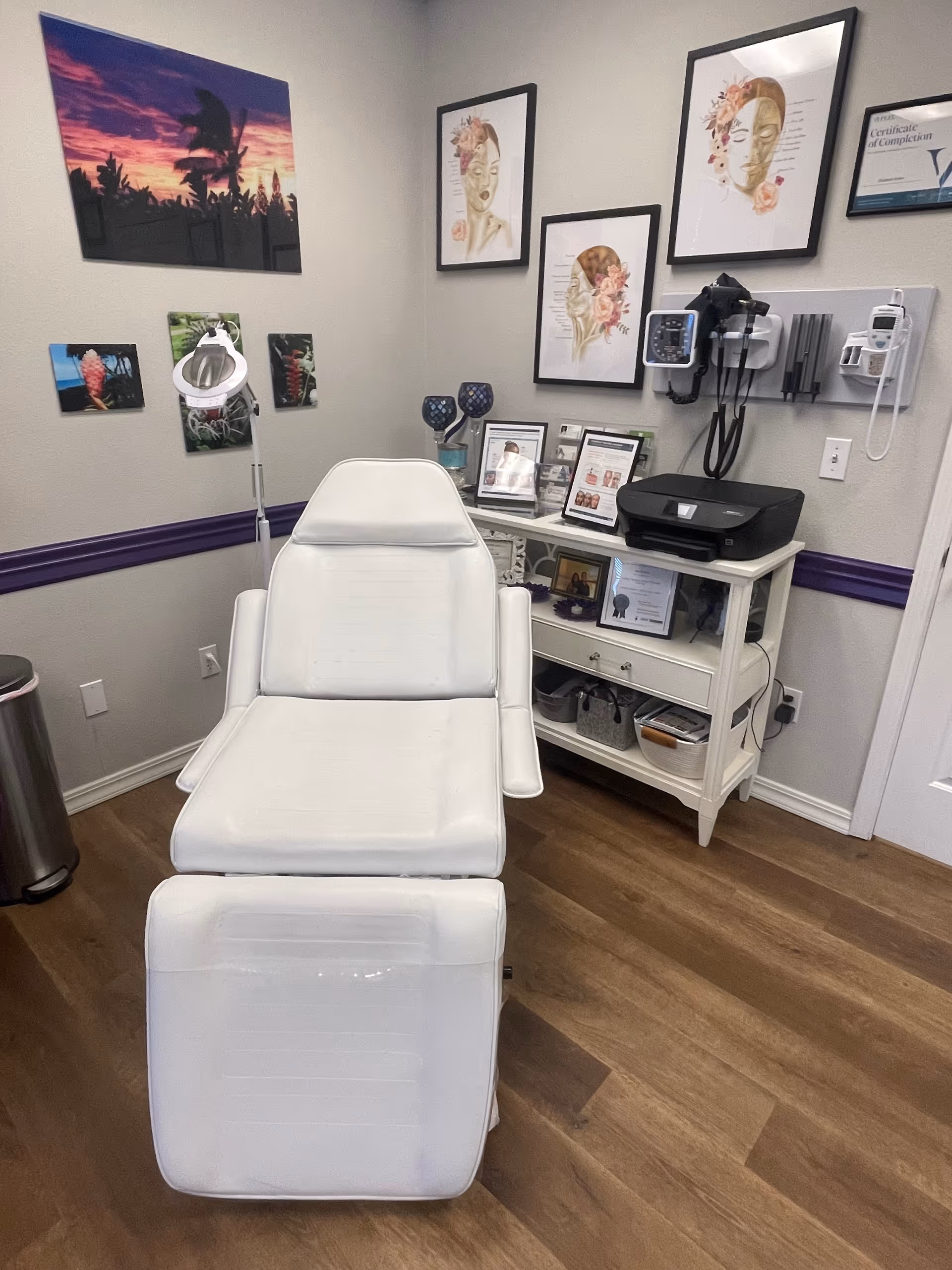 White reclining treatment chair in a clinic-like room with medical equipment and framed art.