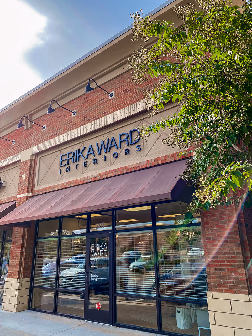 Brick storefront with blue ERIKAWARD INTERIORS sign and large glass doors.