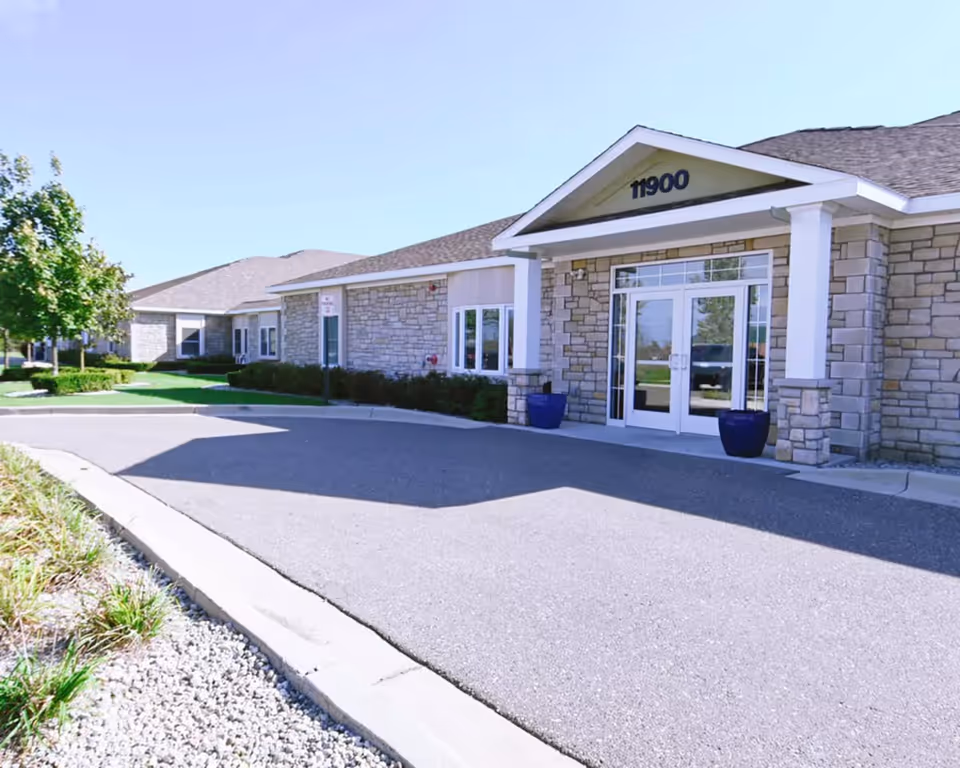 Stone-clad senior living facility entrance with glass doors and landscaped front walkway