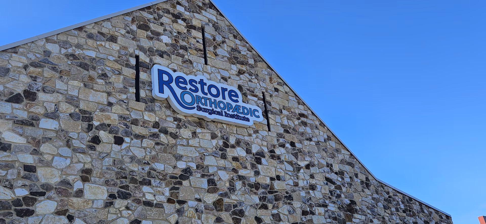 Stone facade of a building with a Restore Orthopaedic Surgical Institute sign.