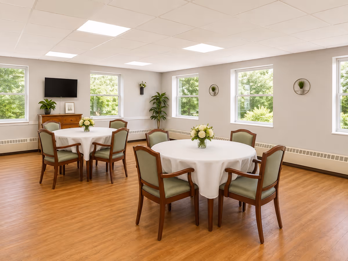 Bright dining room with round tables, white tablecloths, and green upholstered chairs.