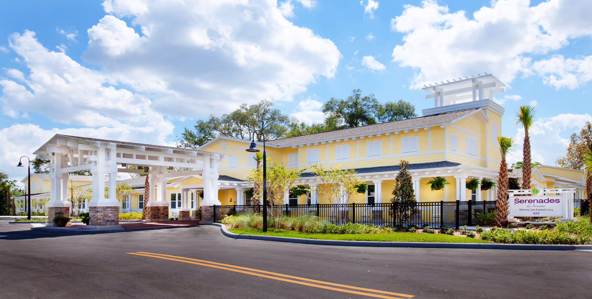 Exterior view of a yellow assisted living facility with a gated entrance and landscaping.
