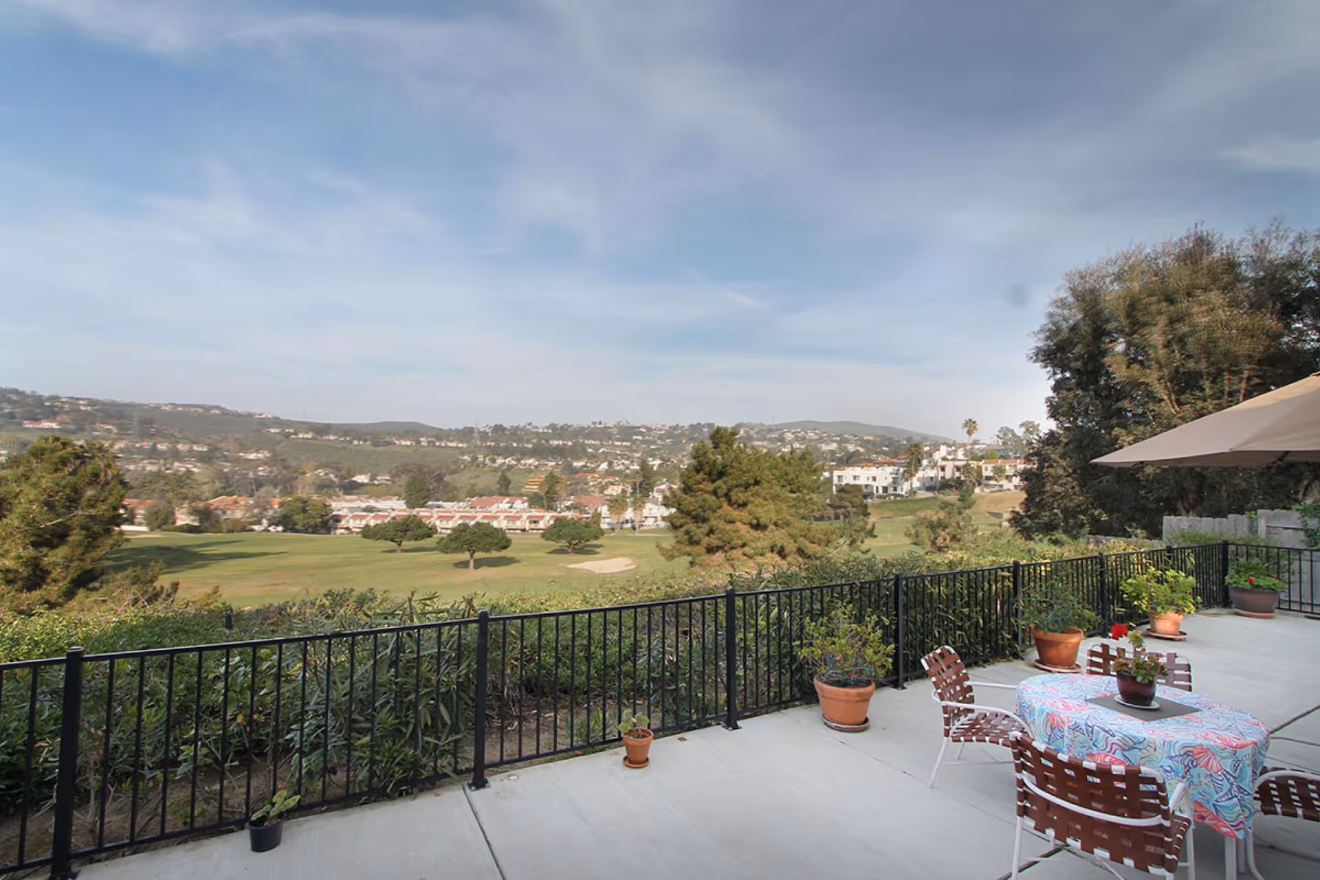 Outdoor terrace with table, chairs, potted plants, and a hillside view.