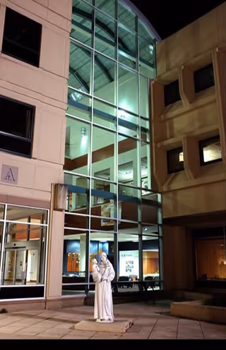 Night view of St Anthony Regional Hospital exterior with glass facade and white statue near entrance.
