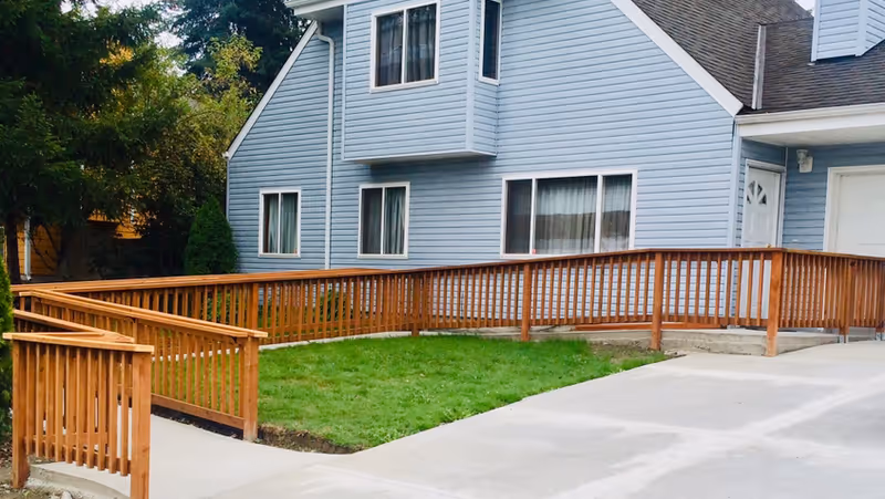 Blue multi-story home with wooden ramp railing and concrete driveway in foreground.