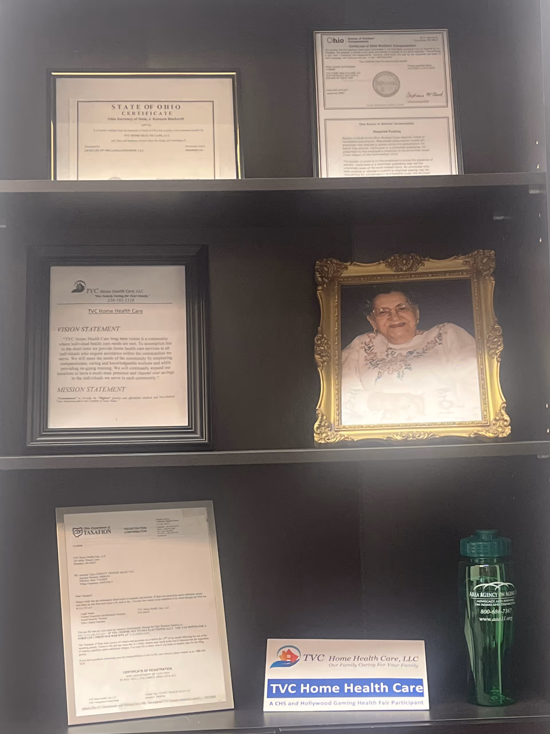 Shelf with framed certificates, a gold-framed portrait, and a TVC Home Health Care sign.