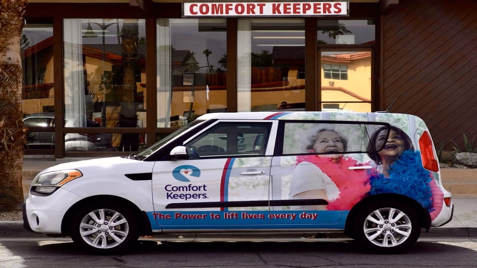 A Comfort Keepers branded vehicle parked in front of a building with large windows.