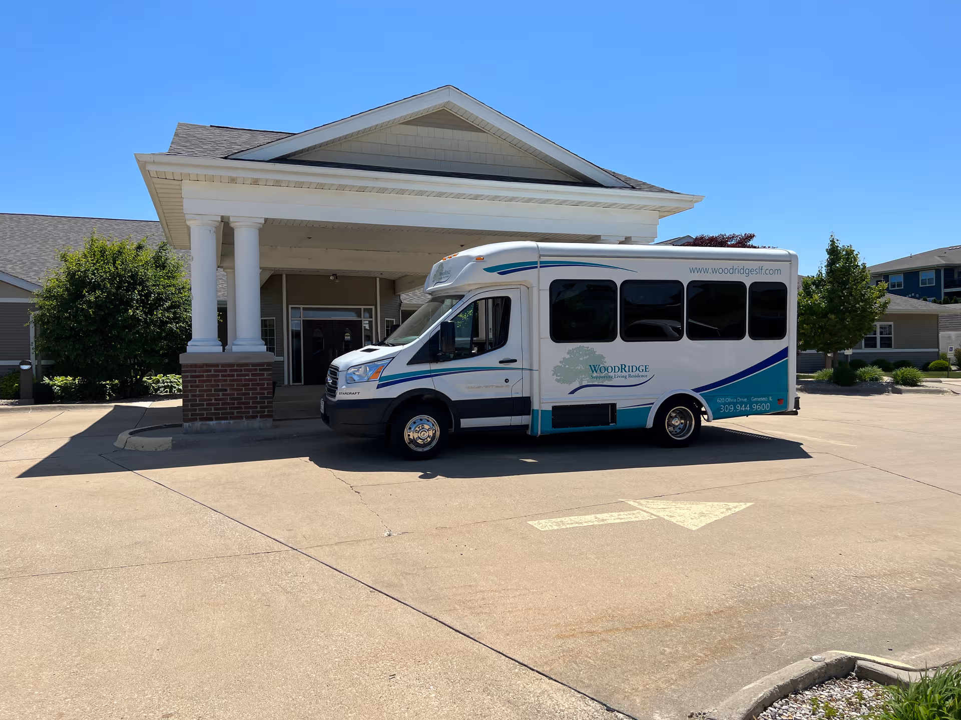 White building with columned entrance and a WoodRidge shuttle bus parked in front.