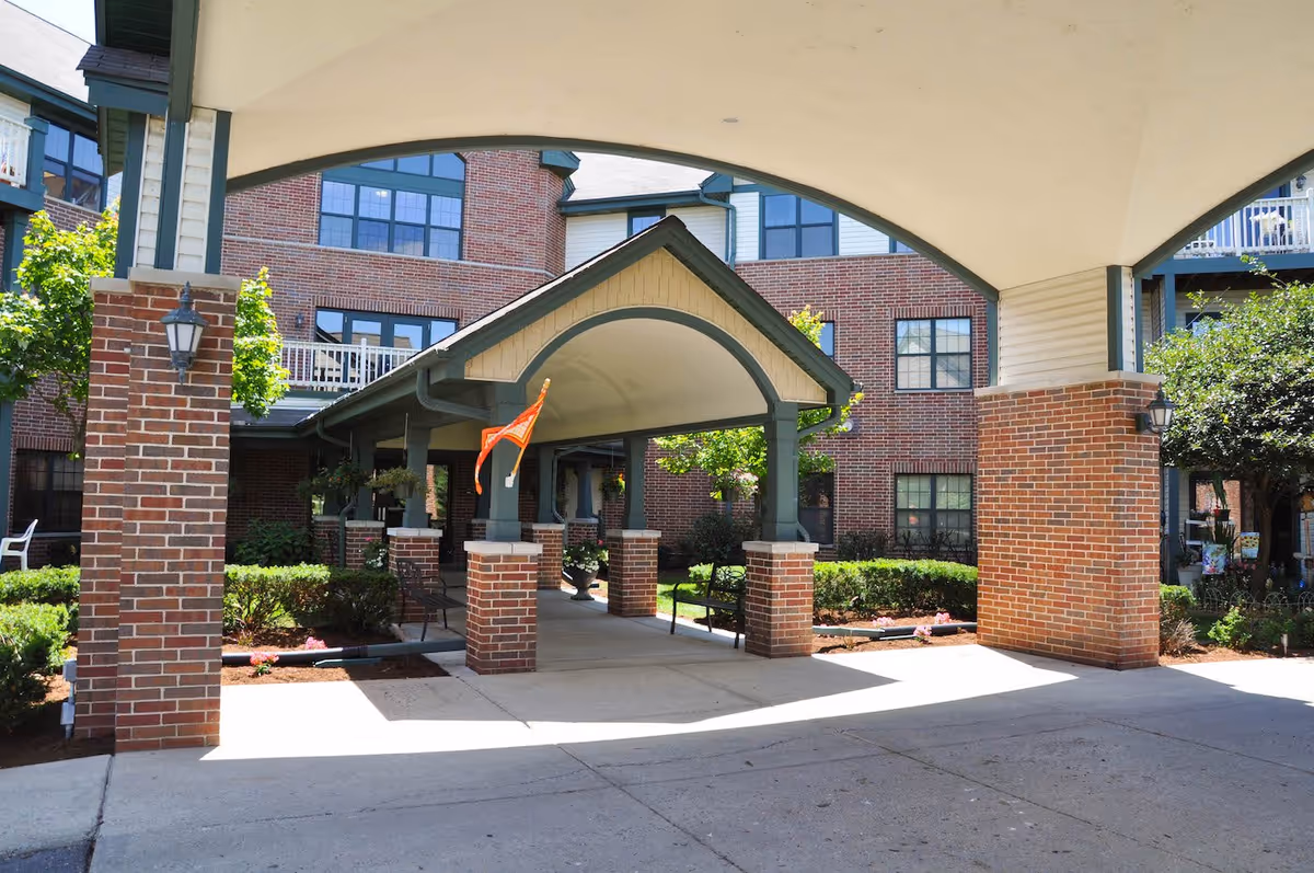 Covered porte-cochere entrance with brick pillars and an arched canopy in front of a multi-story brick senior living building.
