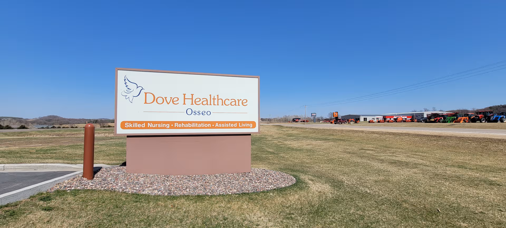 Wide outdoor view of a Dove Healthcare Osseo sign on a grassy lot with distant vehicles
