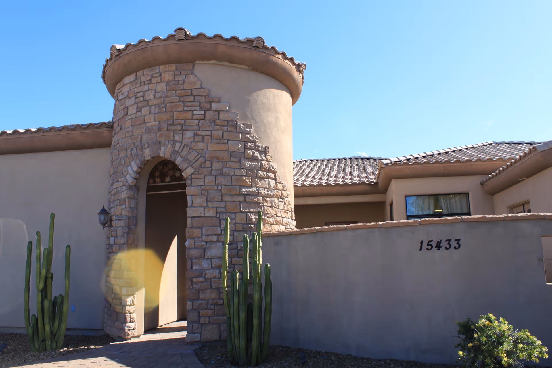 Desert-style building exterior featuring a round stone tower entrance and tall cacti.