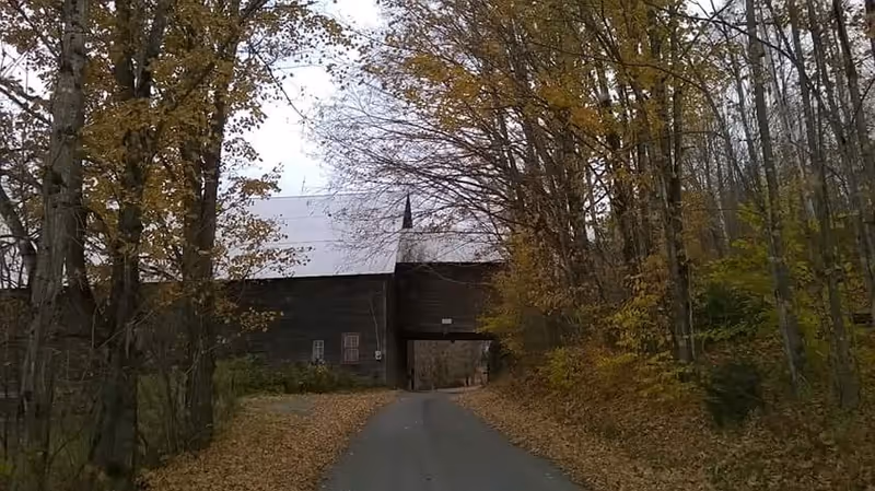 Exterior view of a dark wooden building with an archway amid fall trees.