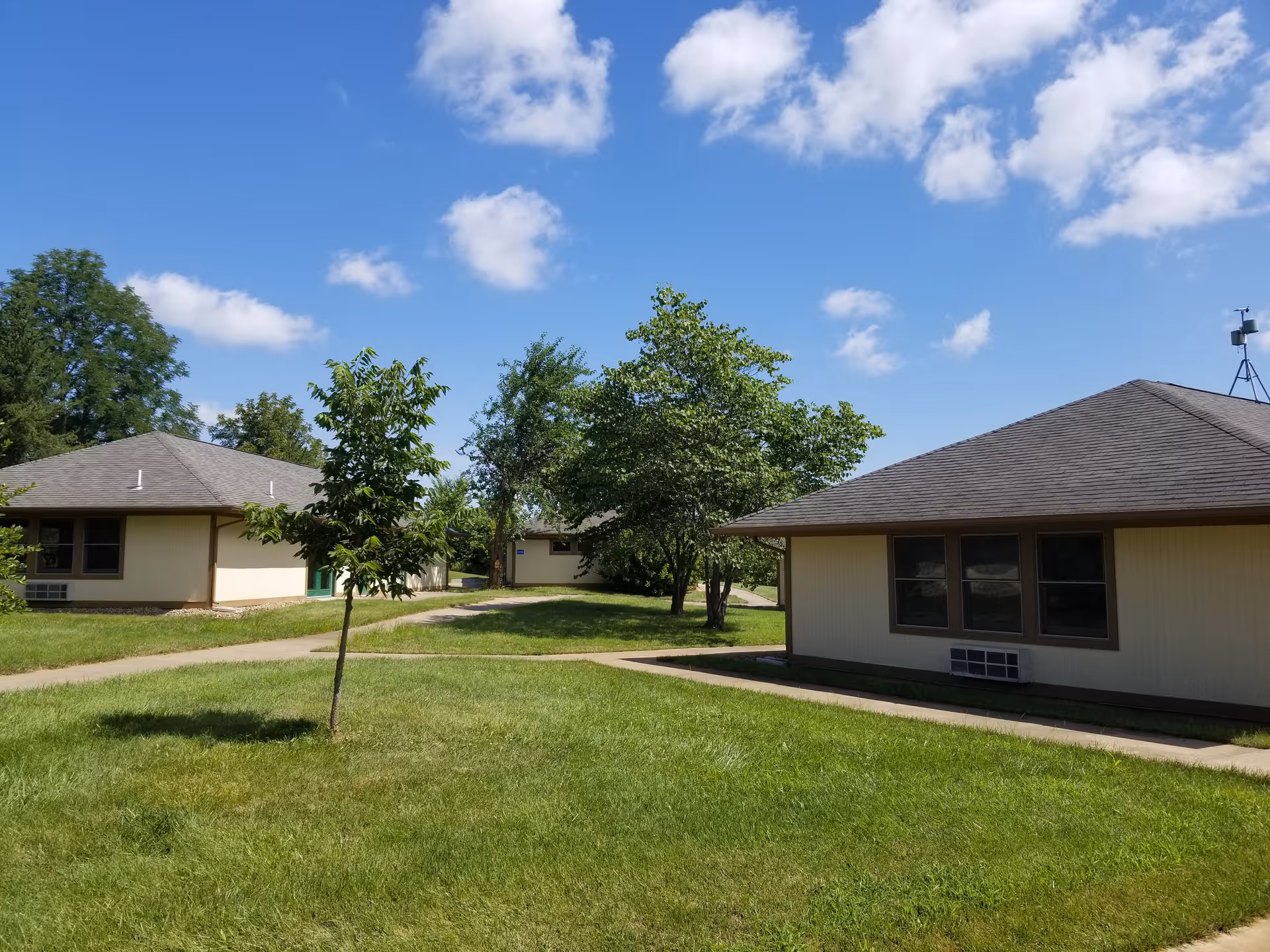 Exterior view of single-story beige buildings with green lawns and trees.