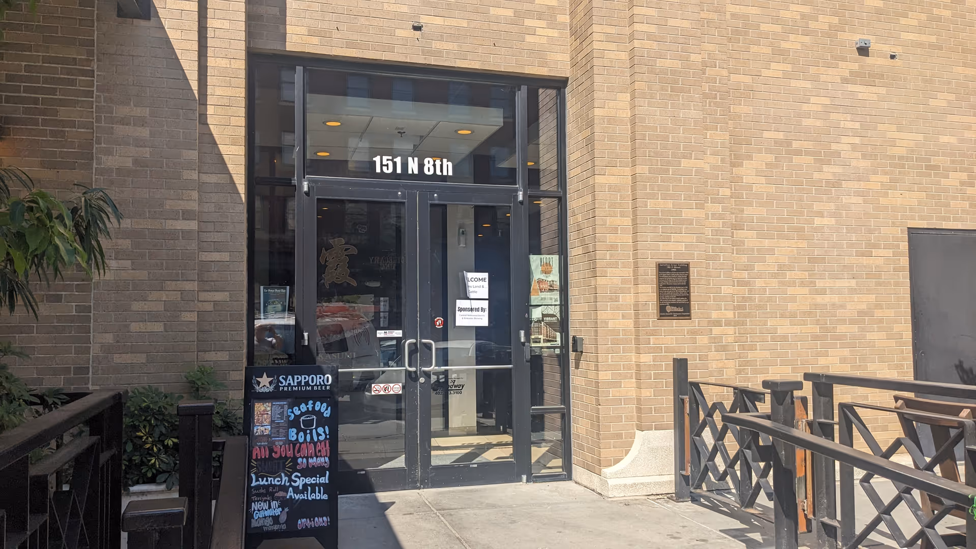 Brick building entrance with glass doors, address plaque, chalkboard, outdoor seating