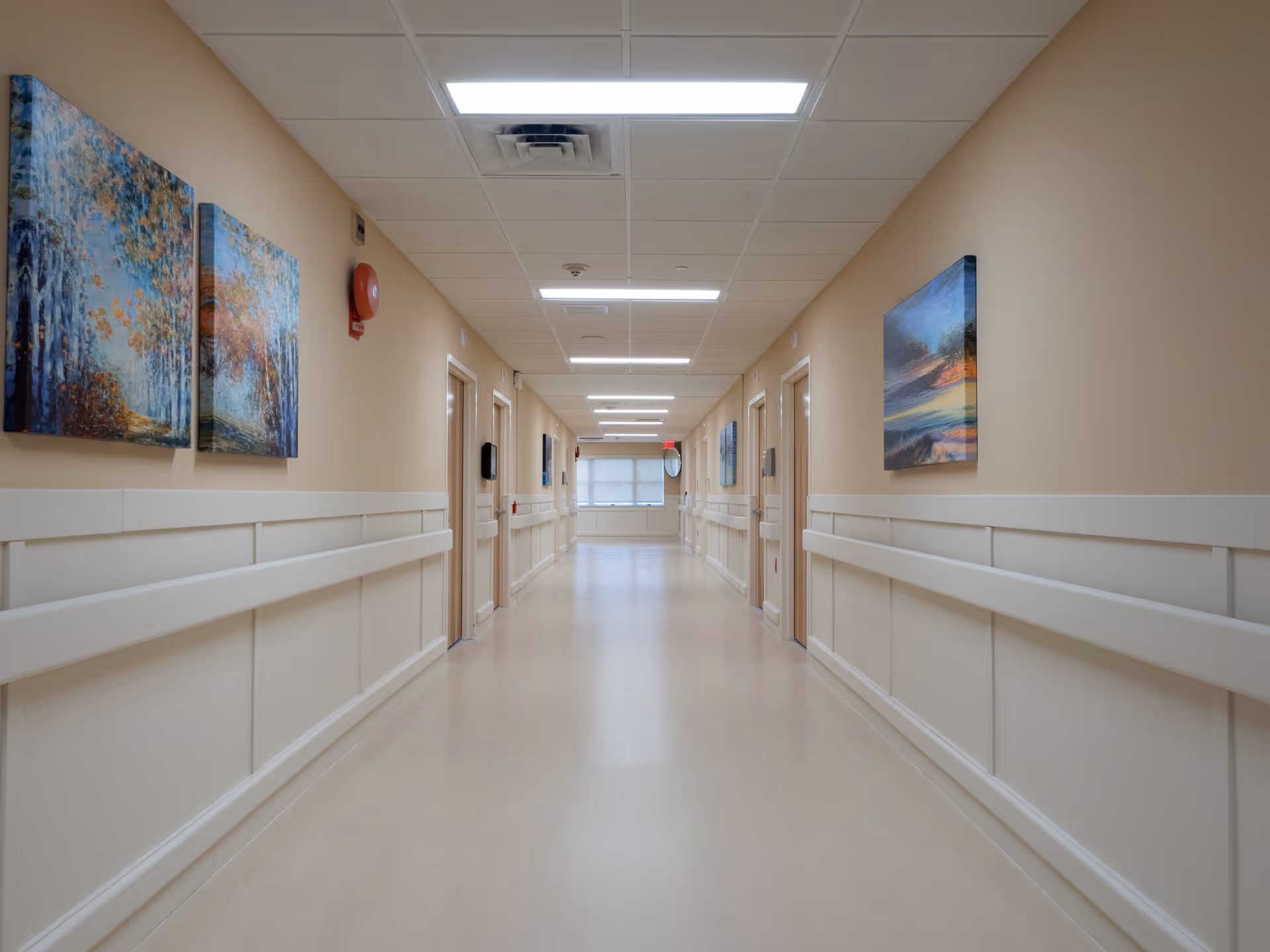 A long, well-lit corridor in a senior living facility with beige walls and art.