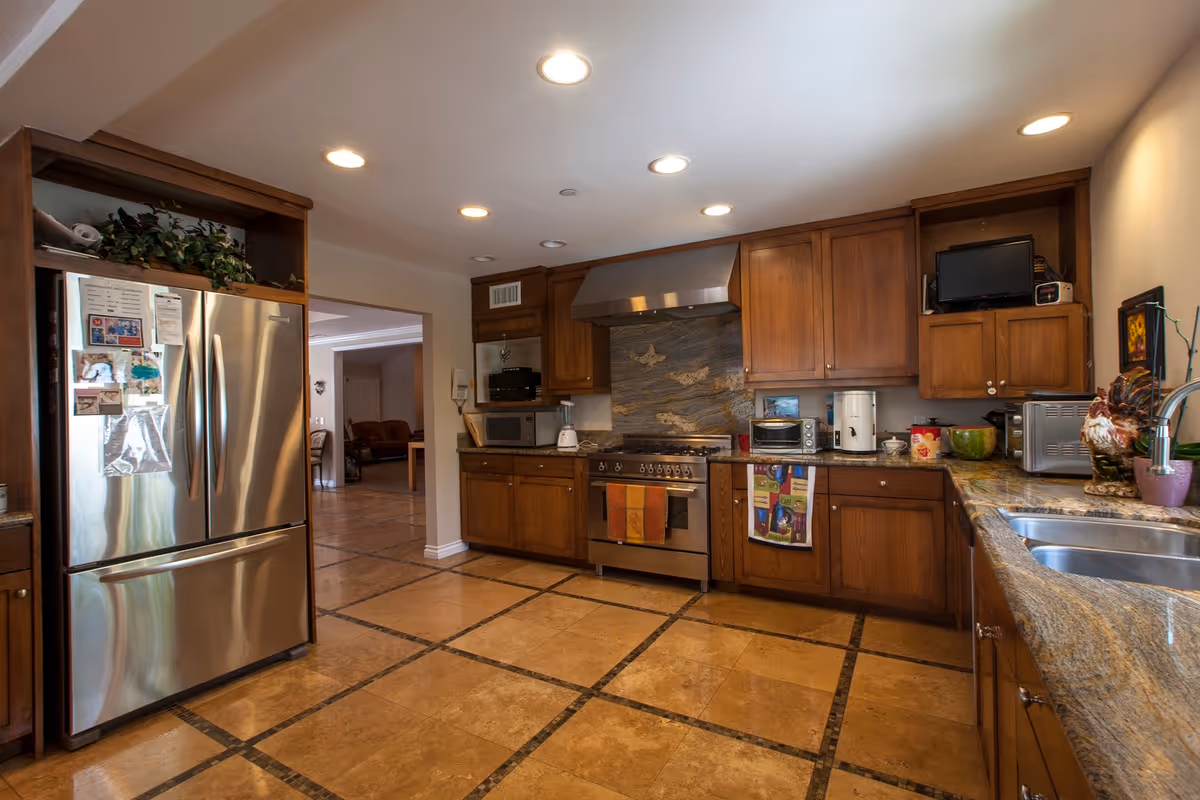 Spacious kitchen with wooden cabinets, stainless steel refrigerator and range, granite countertops, double sink and tiled floor.