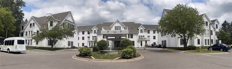 Panoramic view of Ecumen Lakeview Commons exterior: white multi-wing building, entrance, parking, and landscaping.