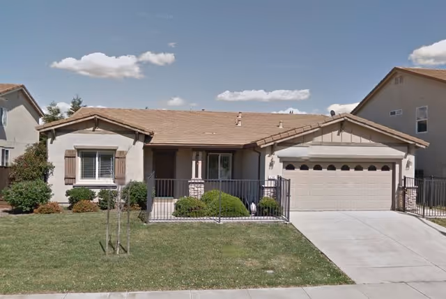 Single-story house with attached two-car garage, front yard, and metal fence.