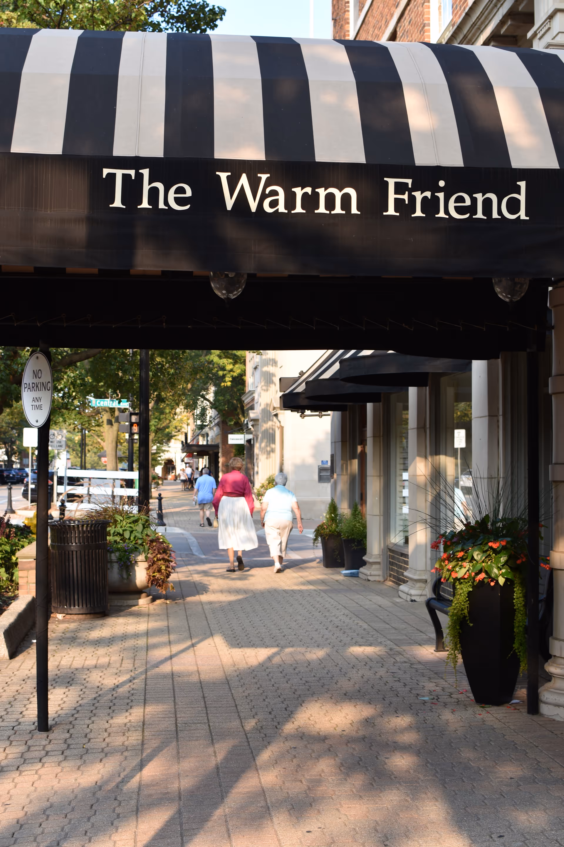 The Warm Friend storefront with striped awning over a pedestrian-friendly sidewalk.