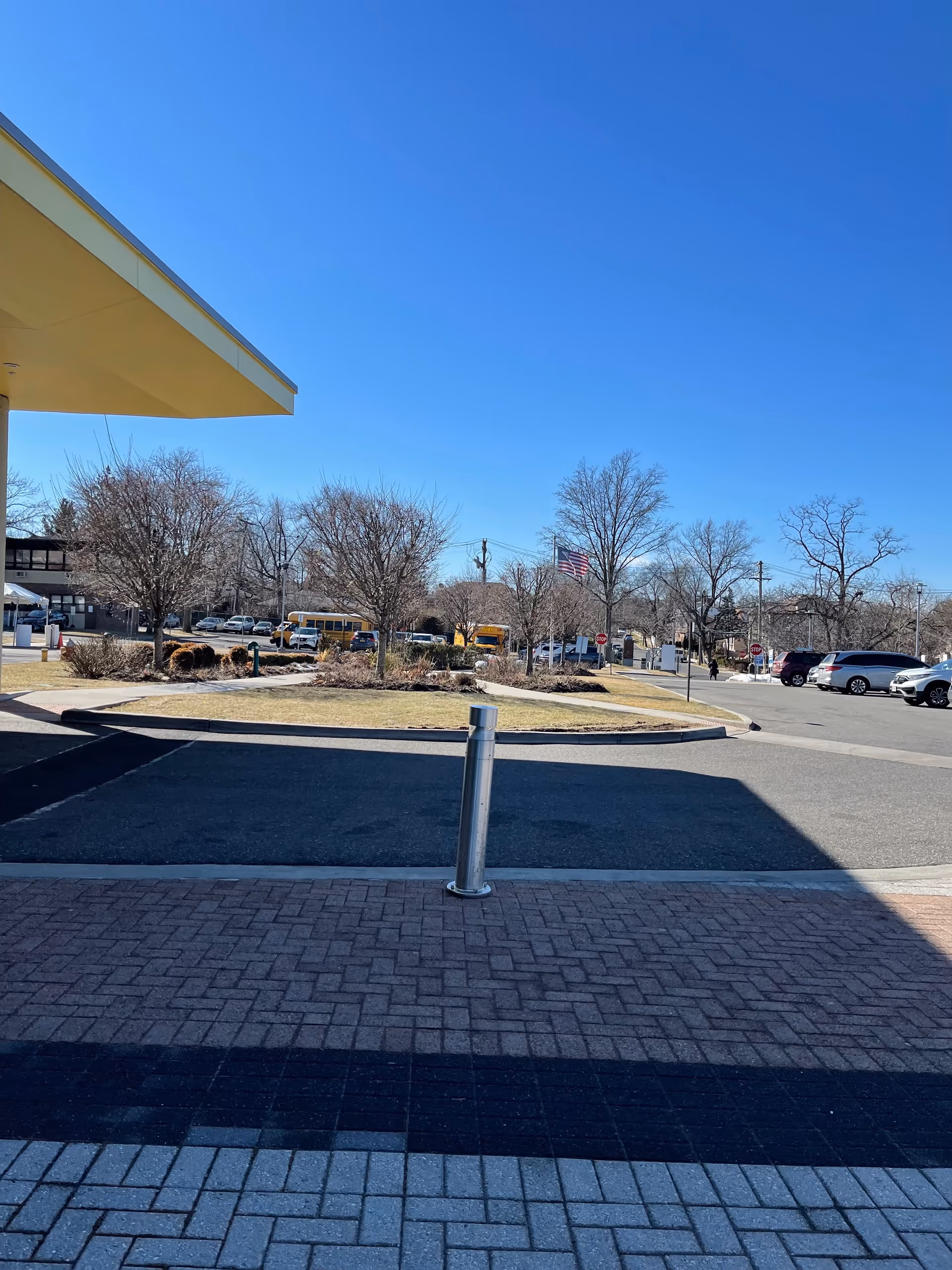 Exterior view of a facility with a driveway, parked cars, and trees under clear blue sky.