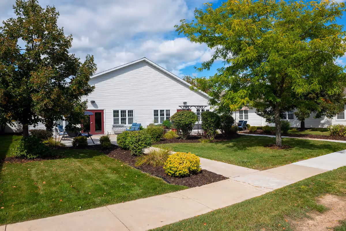 White single-story building with red doors, surrounded by manicured lawn and trees.