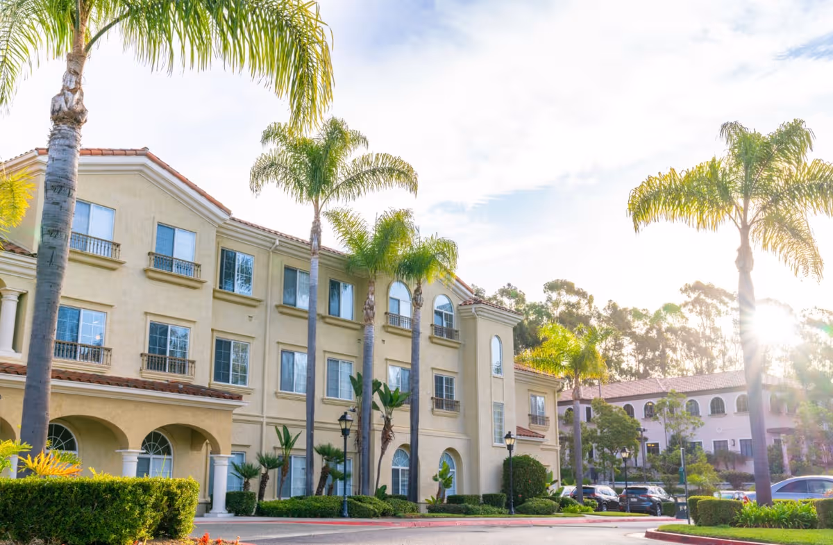 Exterior view of Bayshire Carlsbad facility with palm trees, arches, and parked cars.