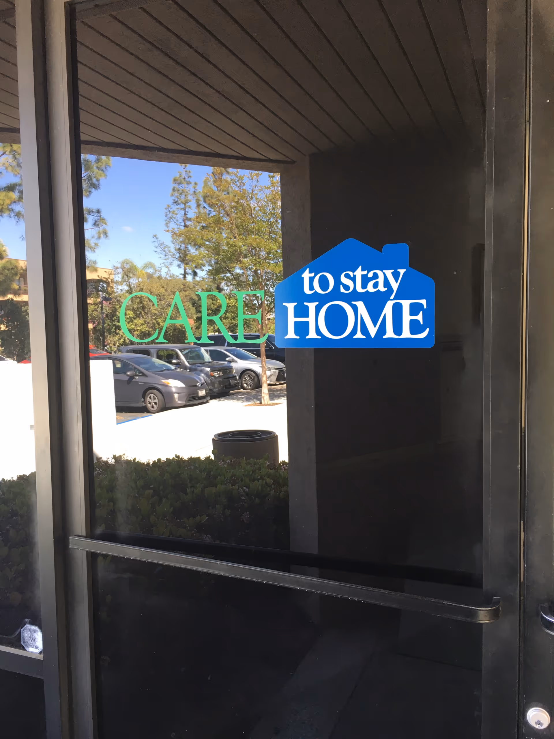 Glass entry door displaying Care To Stay Home logo with parked cars outside.