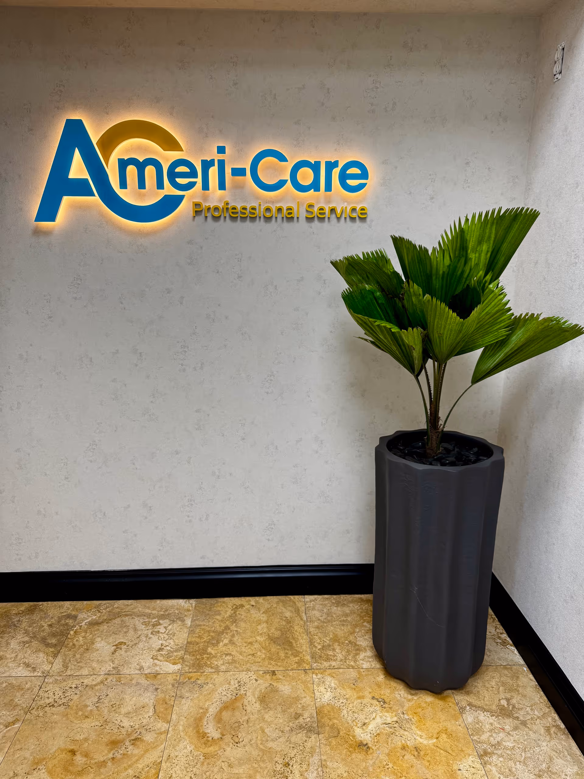 Indoor wall with Ameri-Care Professional Service sign and a tall potted plant.