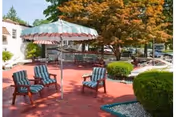 Outdoor patio with red flooring, striped umbrella, and blue chairs around a small garden.