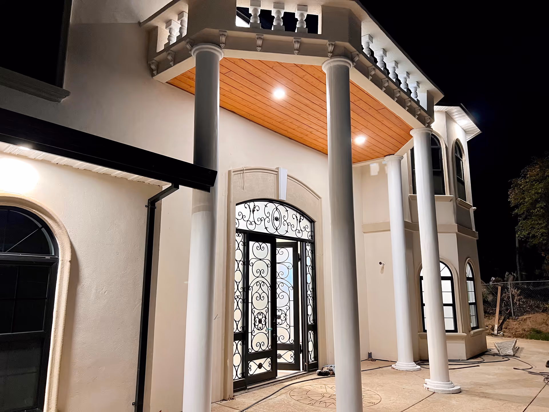 Night view of a grand entrance with tall columns and ornate wrought-iron doors.