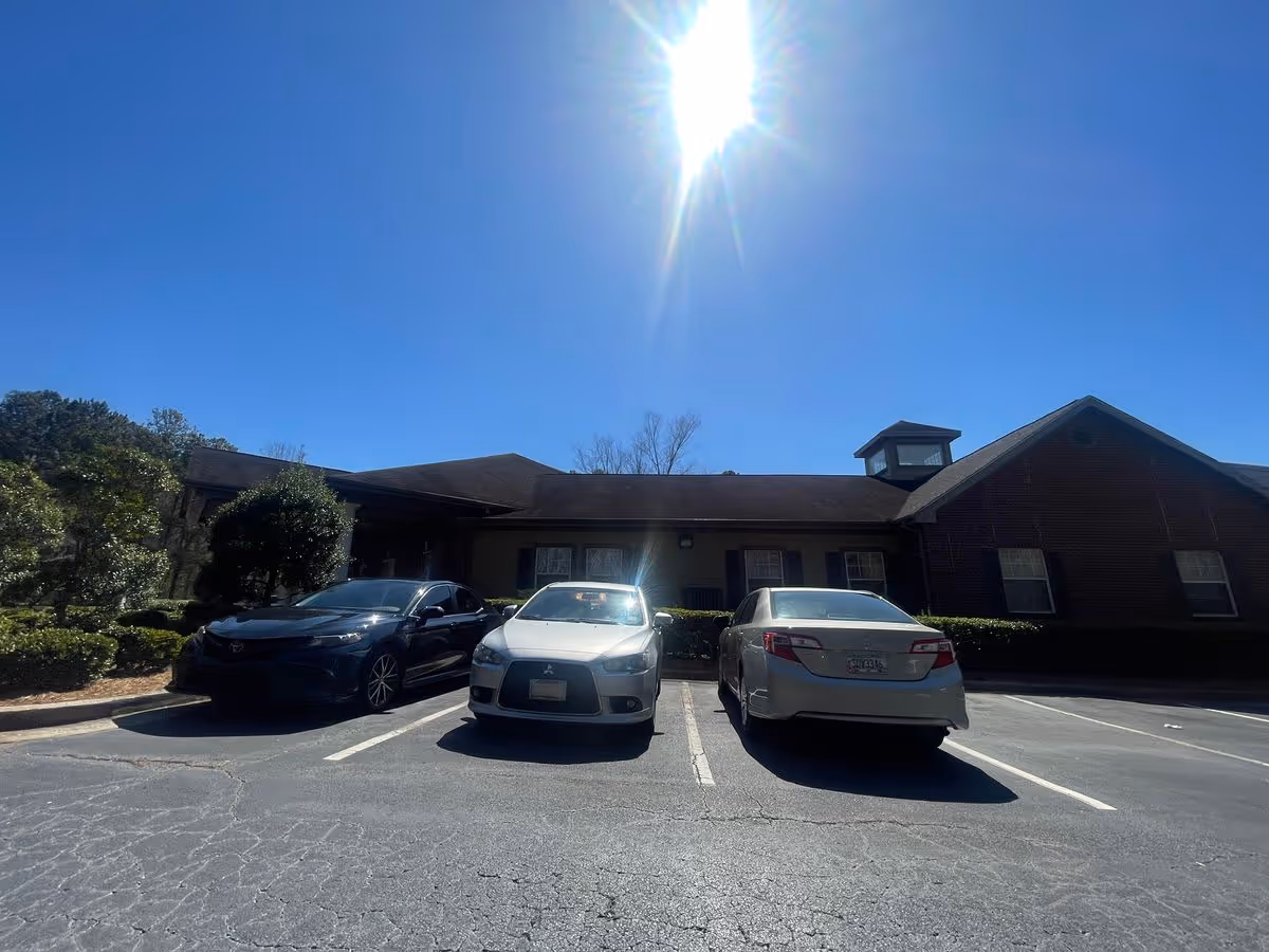 Front exterior of a brick senior living facility with three cars parked in front under a bright sun.